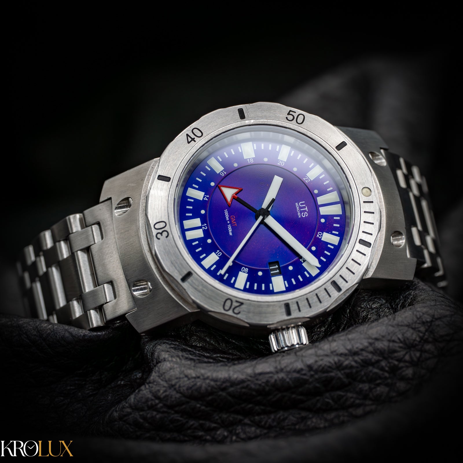 Pillow shot. Silver watch with a blue face on a dark background, featuring the brand 'Krolux'.