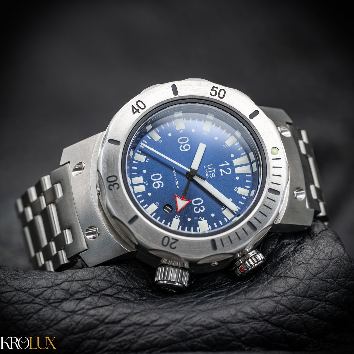 Pillow shot UTS München stainless steel watch with blue dial on a dark background, featuring the brand 'Krolux'.