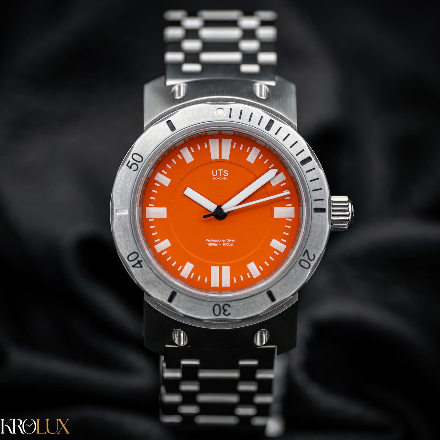 Hero Shot UTS München A stainless steel wristwatch with a vibrant orange dial and a matching orange bezel, featuring a silver-toned metal link bracelet. The brand name 'UTS' is visible on the dial.